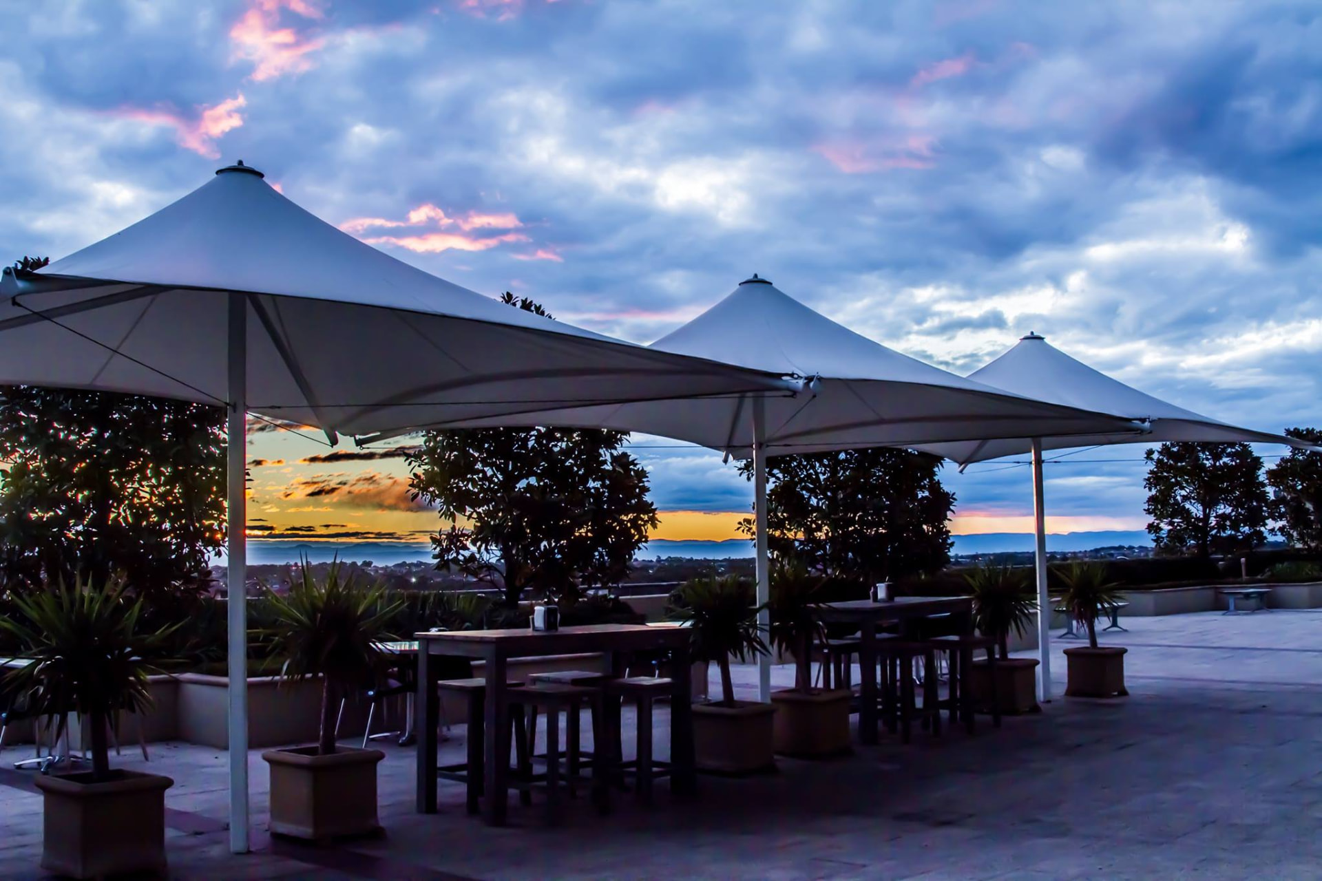 White canopy umbrellas over terrace tables at sunset with pink clouds